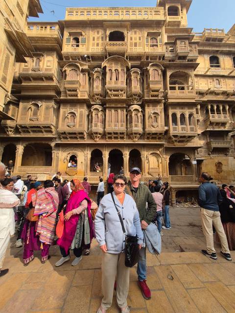       Two people posing in front of an intricately carved sandstone building with a crowd.
  