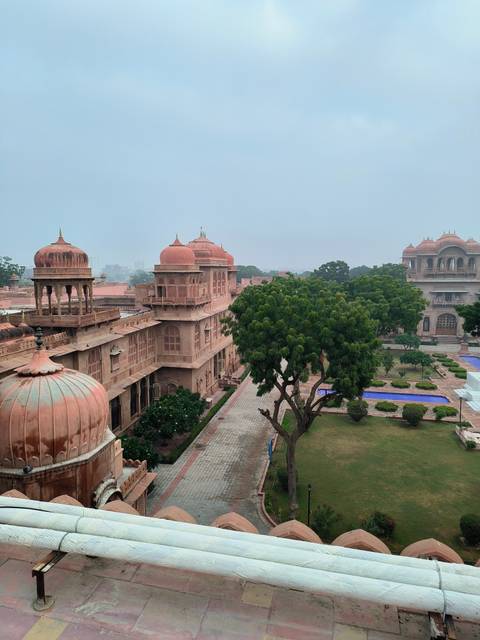       Red sandstone palace with gardens and trees in front.
  