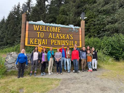       Group posing in front of a 'Welcome to Alaska's Kenai Peninsula' sign.
  