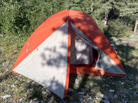       Orange tent set up in a forested area.
  