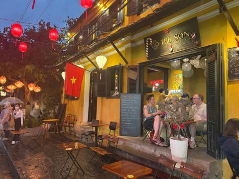       People sitting at a small bistro with Vietnamese decor in the evening.
  