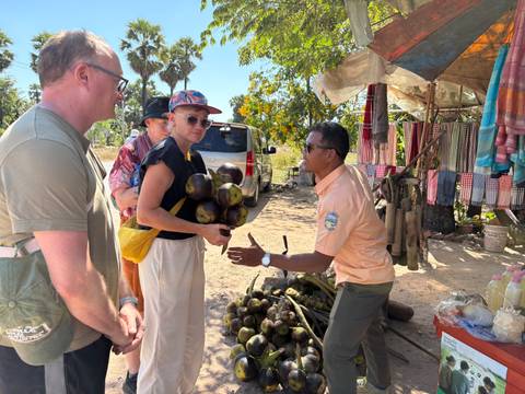       Tourists interacting with a local vendor holding coconuts.
  