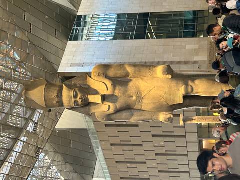       A large statue of an ancient Egyptian pharaoh indoors with visitors.
  