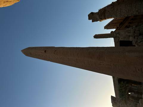       An ancient obelisk with hieroglyphics against a blue sky.
  