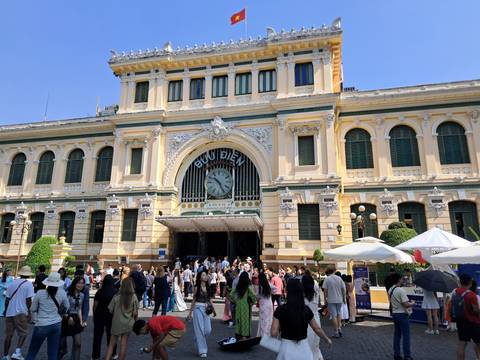 Historic building with a large clock and many people gathered outside on a sunny day.