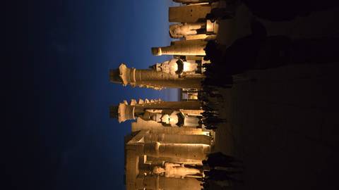 Illuminated ruins of a temple with statues at night.