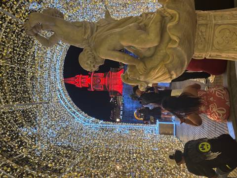 Illuminated statue and people in front of a lit-up clock tower at night.