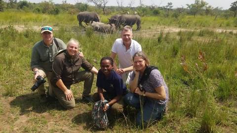 Group of people posing with rhinos in the background