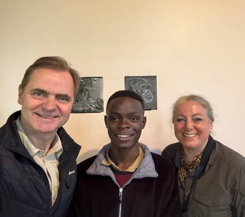 Two people smiling indoors with a drawing of chimpanzees in the background.
