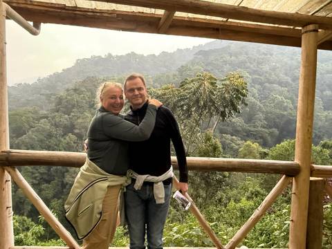 Two people embracing on a wooden balcony with dense forest in the background.