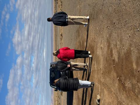 People walking towards a black van in a desert area.