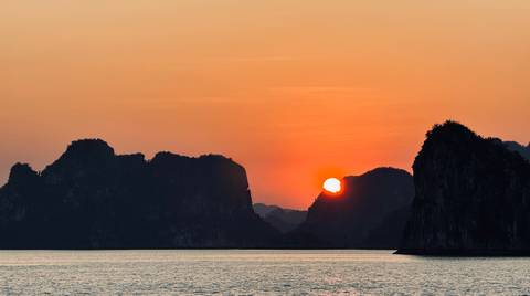       Sunset view over karst landscapes and water, creating a silhouette effect.
  