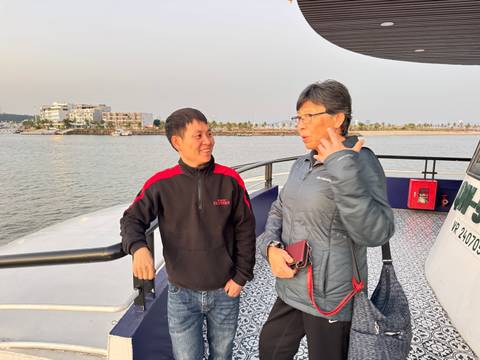       Two people standing on a boat deck with water and buildings in the background.
  