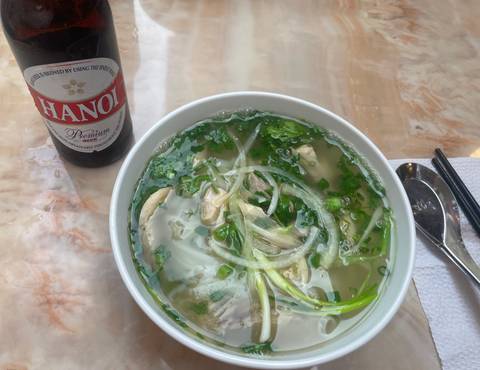       Bowl of pho and a bottle of Hanoi Premium beer on a table.
  
