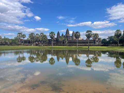       Angkor Wat temple reflected in water surrounded by palm trees.
  