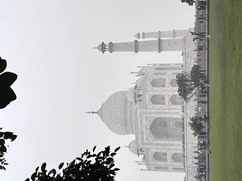 The Taj Mahal, partially obscured by fog, with visitors in the garden.