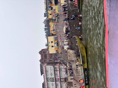       Ghat along the river with people performing rituals and boats nearby.
  