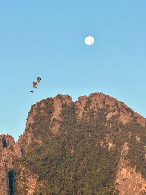 Microlight aircraft flying beside a rocky mountain.