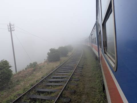 Train moving through foggy landscape on train tracks.
