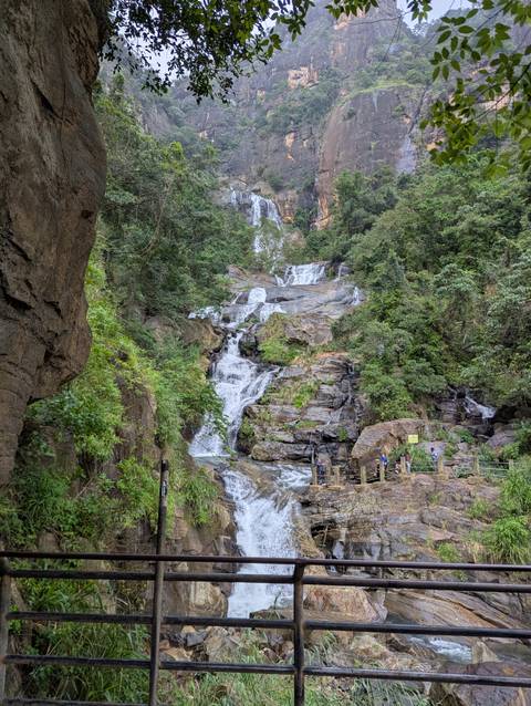 Waterfall cascading down rocky slopes with people observing.