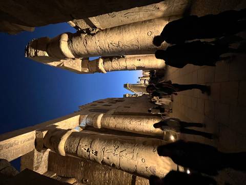 Ancient Egyptian temple illuminated at night with people walking around.