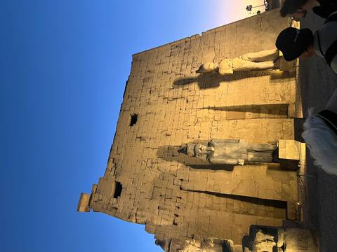 Statues at an Egyptian temple with hieroglyphs lit up at dusk.