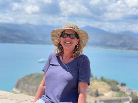       Woman posing with a hat in front of a coastal view.
  