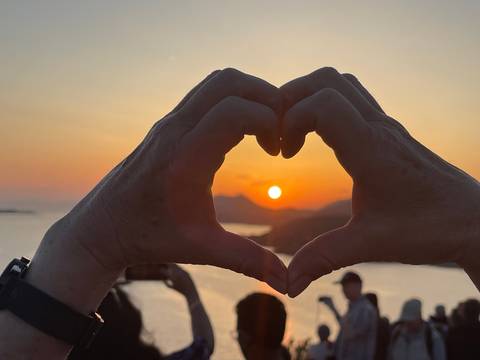       Hands forming a heart shape against a sunset skyline.
  