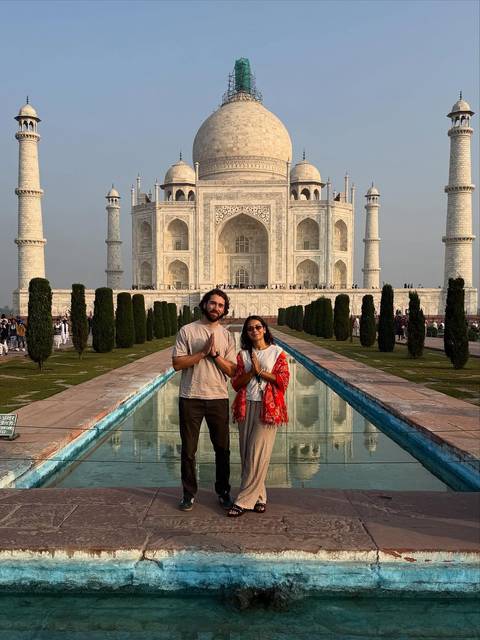 Two people posing in front of the Taj Mahal with the reflecting pool.