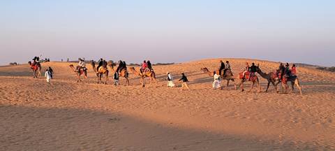       People riding camels across sand dunes.
  