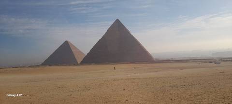       Two pyramids in the desert with a hazy sky.
  
