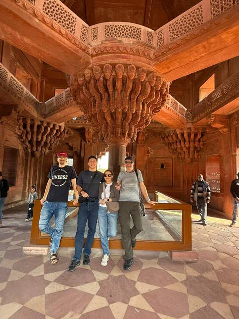 Four people posing in front of an intricately designed sandstone structure.