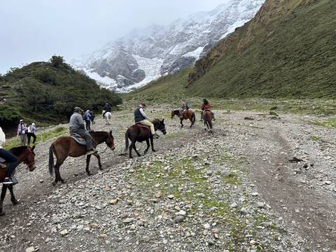       People on horseback riding towards a snow-covered mountain.
  