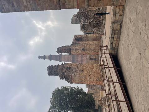 Ancient minaret surrounded by ruins and cloudy sky.