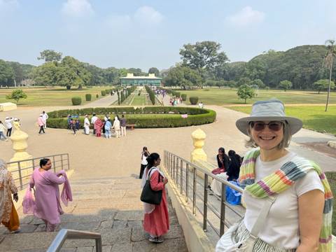       A smiling woman standing on steps in front of an expansive garden.
  