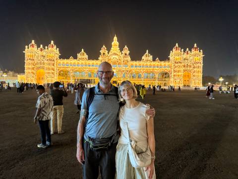       A couple standing in front of a brightly lit palace at night.
  