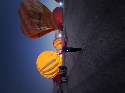 Elderly woman standing near hot air balloons at dawn.