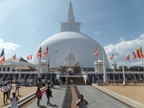 White stupa with flags and people gathered around.