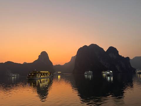 Cruise ships in a bay at sunset with limestone islands.