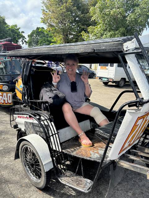 Person sitting in a tricycle taxi holding up peace signs.