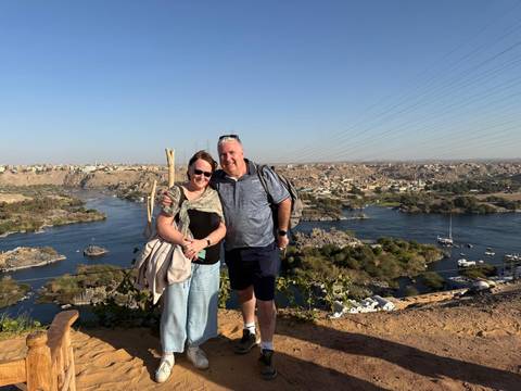 Two people posing with a river and landscape in the background.