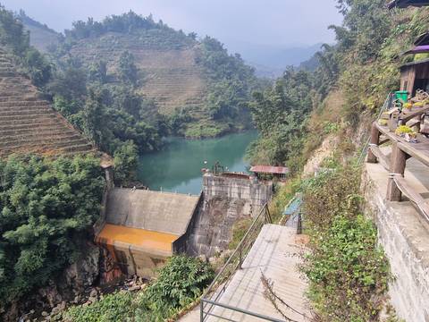       Scenic canyon view with a dam and a river flowing through dense forest.
  