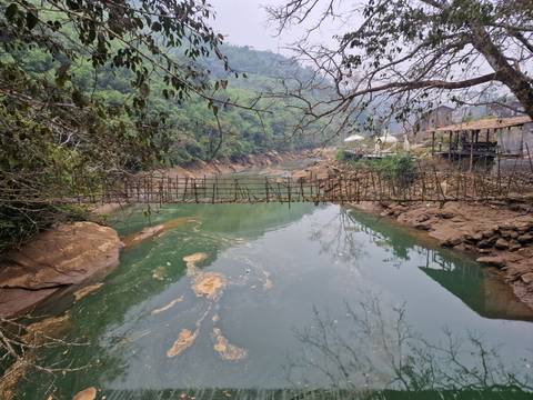 A bamboo suspension bridge spans a river with rocky banks.