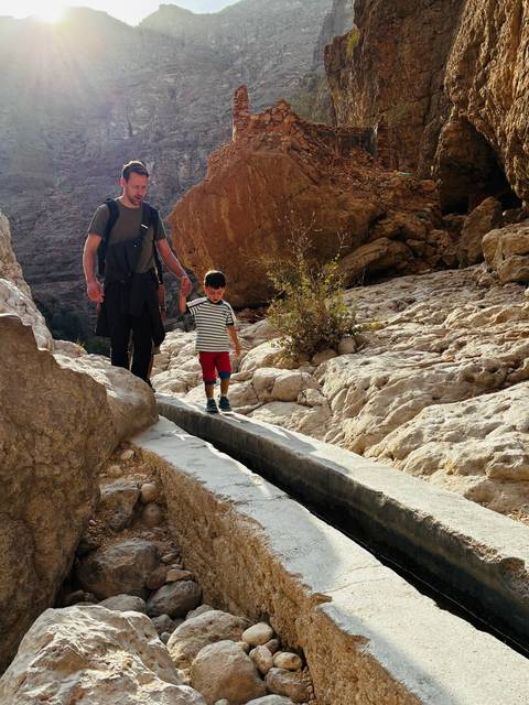       Child walking alongside an adult on rocky terrain.
  