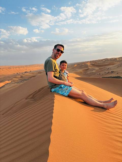       Man and child sitting on a sand dune enjoying the view.
  