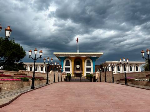       Grand palace with dramatic sky, showing flags and flowers.
  