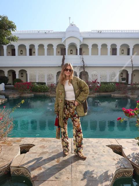 A woman posing in a garden with a pool in front of a decorated building.