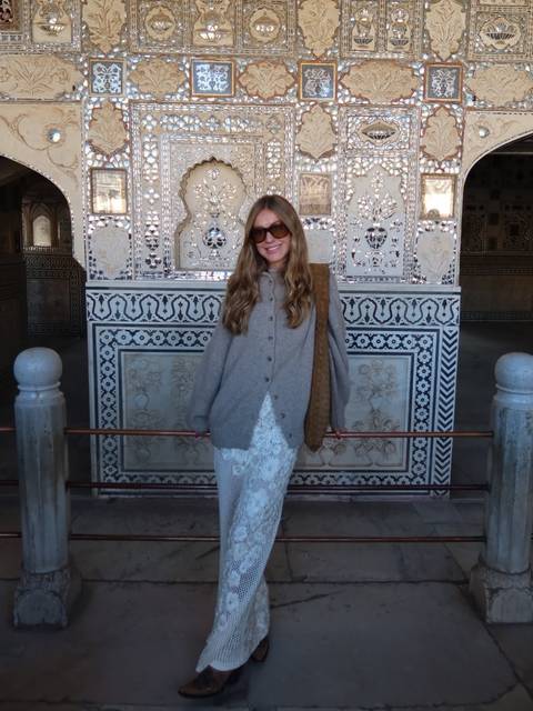 A woman in front of an intricately decorated wall inside a historic building.