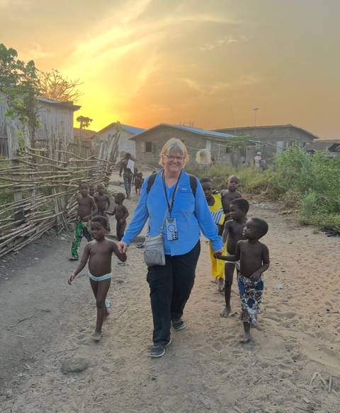 Woman walking with children in a rural village at sunset.
