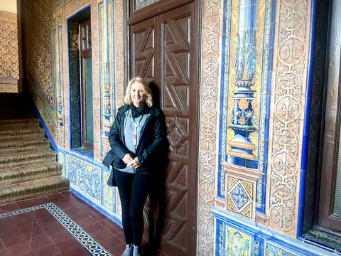 A woman standing in front of intricate tiled walls in a historic setting.